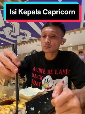A man is seated at a table with food in front of him, holding chopsticks. The background features a restaurant setting with soft lighting and decorative elements. A text overlay in a rectangular banner sits above the man's head.