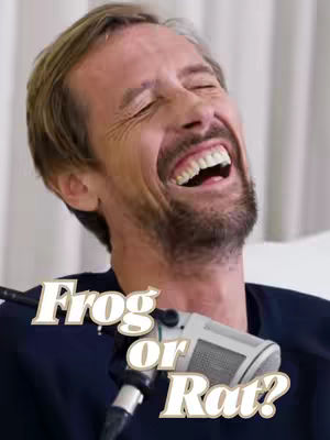 A man with a beard laughs with his eyes closed. A text overlay with the words “Frog or Rat?” is in front of him, sitting by a microphone.