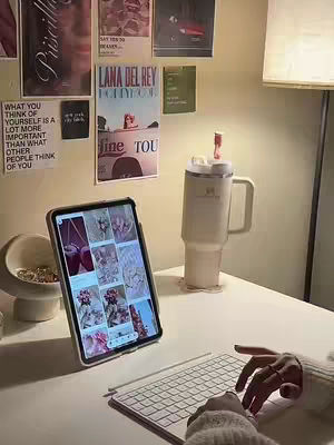 The cover image shows a well-lit desk setup with an iPad, keyboard, and a large tumbler. Several posters hang on the wall behind it, and the scene has a warm, inviting aesthetic. A person's hands are visible, typing on the keyboard.