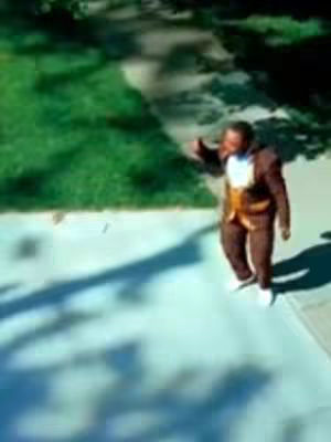 The cover image shows a man walking on a concrete path in what seems to be an outdoor setting. He is wearing a brown suit with a lighter-colored shirt and vest underneath, and white shoes. To his left is a grassy area, while the path he walks on casts a long shadow.