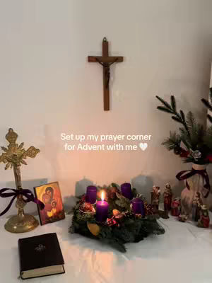 A white table is set with an Advent wreath with purple candles, a Bible, an icon, and other religious items. A traditional Advent scene.