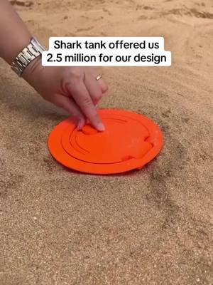A close-up shot shows a hand with a silver watch and ring touching an orange circular object on a bed of sand. Text overlayed says, 'Shark tank offered us 2.5 million for our design.'