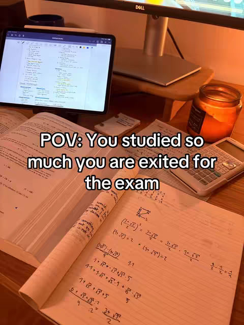 The image shows a close-up of a desk with various study materials. A tablet displaying notes is positioned prominently, alongside visible open books. A calculator and a candle are also present, suggesting a study environment. The warm lighting and the presence of study materials implies study content.