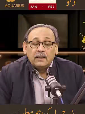 The cover image features a man in glasses and a button-up shirt appearing to be on a video call. Above his head there is a text overlay with a sign that includes "AQUARIUS" on the left and additional text in a language I can't identify, along with the time frame "JAN - FEB". A microphone is positioned in front of him. He has a mustache. The background is blurred, suggesting a professional setting such as a studio.