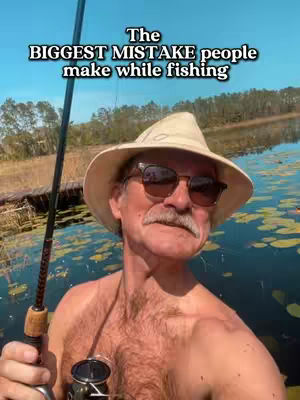 An older man in a straw hat and sunglasses is holding a fishing rod while posing in a boat on a lake. Text on the image reads: "The BIGGEST MISTAKE people make while fishing". The background shows a forest and clear, blue sky.