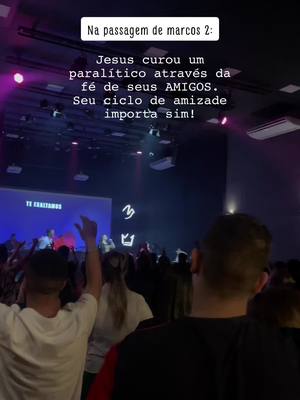 An interior shot of a church during an event, with a crowd of people and a stage in the background. Text overlayed at the top says "Na passagem de marcos 2:". A light blue screen is displayed behind a person with their arm raised.