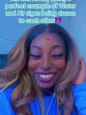 A close-up shot of a woman with long, wavy blonde hair, smiling widely. She is wearing a blue garment with a white earpiece. Above her forehead is a magenta dot. The background is blurred, suggesting an indoor setting with blue tones. Text overlayed on the top.