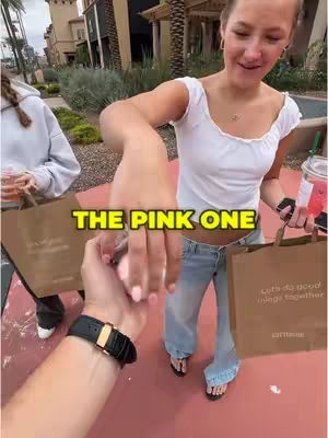 A first-person perspective of a person holding hands with someone else and shopping bags. The main person of the image is a female. The text overlay says "THE PINK ONE".