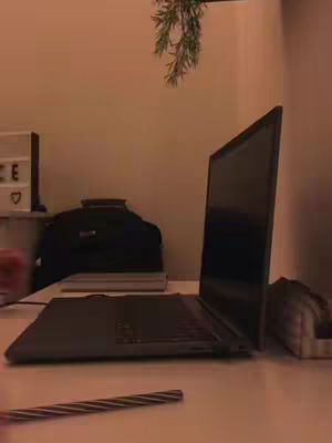 The cover image shows a home office setting with a laptop open prominently positioned on a desk. A pen lays in the foreground. Behind the laptop, a black computer bag is visible on the desk. In the background, a decorative illuminated sign rests on a shelf. The overall color scheme is muted, with warm lighting casting shadows.