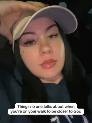 A selfie-style shot featuring a woman wearing a light-colored visor cap, covering her hair. She fills most of the frame, with a portion of her hand visible near the cap. Her face is lit with what appears to be a pink light on one side and natural light on the other, accentuating her features, including her dark hair and visible eye makeup. A text box at the bottom contains white text against a black background.
