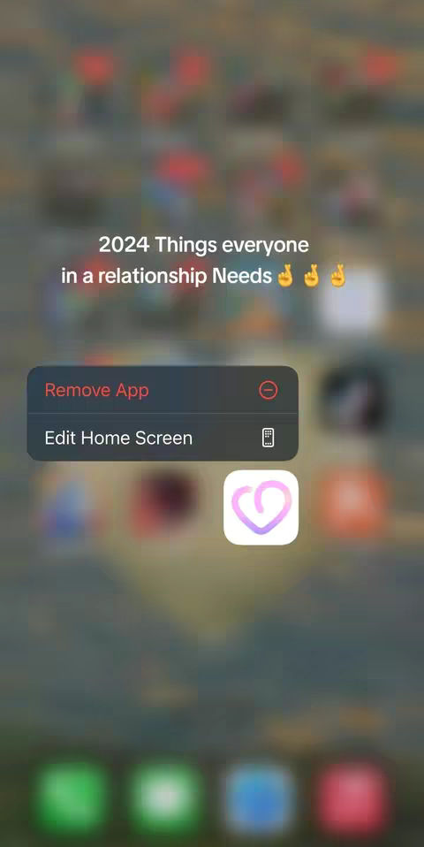 The cover image shows a phone screen with a blurry background of what appears to be a cityscape. The foreground features several app icons, with a pop-up asking to Remove App or Edit Home Screen. The main text reads: '2024 Things everyone in a relationship Needs' with the hands of the blessing emoji.