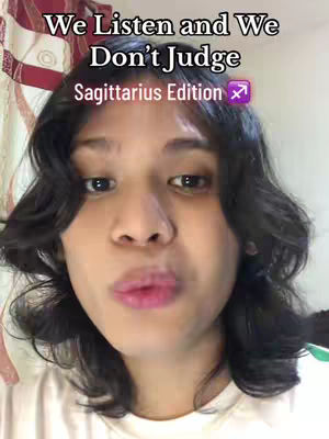 A selfie-style image featuring a person with dark, wavy hair. The person is looking directly at the camera. The background is blurred.