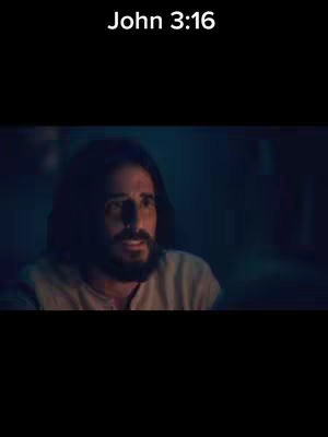 A medium shot of a man with long hair and a beard, lit from the side in a dimly lit area. The text "John 3:16" is at the top of the frame.