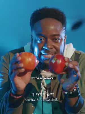 A man of African descent holds an apple in each hand, smiling at the camera. The background is blue, and text overlays read '#SYMPTOMS' and 'SERMON: HE'S BEING BUILT'. Below, in a smaller font, it says: 'IT'S THE APPEARANCE'.