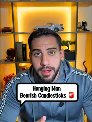 A man is centered in the frame, facing the camera and speaking. He has dark hair and a short beard and is wearing a gray hoodie. A speech bubble overlay contains the text 'Hanging Man Bearish Candlesticks' and a red data icon.