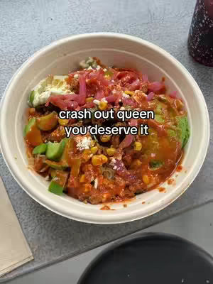 The image shows a top-down shot of a bowl filled with food. The bowl is off-white and contains a mix of ingredients, including what appears to be avocado, red onions, corn, and a red sauce. There is text overlayed on the image.