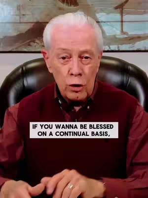An older man with short, gray hair is seated, facing the camera. He is wearing a burgundy vest and a white shirt. A text overlay appears in a white box with black text. Behind him, there is a dark, blurred background, which appears to include some artwork.