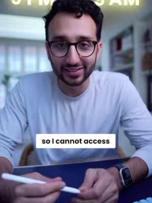 A man with glasses and a beard is holding a white pen in front of a blue desk. A textual overlay reads, 'so I cannot access'. The background shows a cozy living room.
