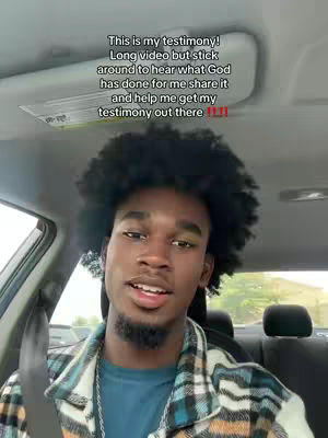A young Black man is seated in the driver's seat of a car, facing the camera. Above him, a text overlay provides context. The man has short, dark, curly hair. He wears a blue shirt under a plaid shirt. Behind him, the car's interior is visible, and the background shows a glimpse of the outside world. The lighting gives a typical daytime feel.