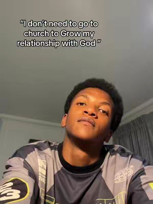 A young Black man looks upward at the camera in a medium shot. He is wearing a dark shirt with a pattern, and a text overlay appears at the top of the frame.
