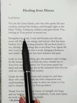 A close-up shot of a page from a book or document. The page is slightly angled and shows printed text. A black pen is placed on the page, and the focus is on text about 'Healing from Illness'. The text is in the center of the frame, with the pen pointing to a specific line within the text. The background consists of a light-colored surface, likely the table.