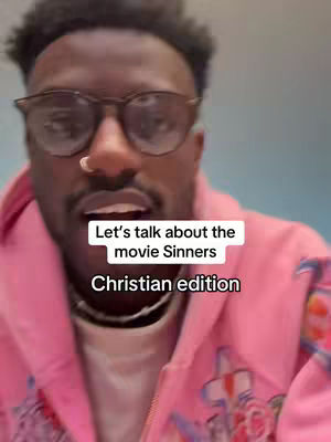 A close-up shot of a Black man wearing glasses and a pink jacket, looking into the camera with an open mouth as if speaking. Text overlays on the image read, 'Let's talk about the movie Sinners Christian edition'. The background is a blurred, light gray.