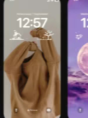 The image shows a person wearing a tan sweater with their arms raised, partially obscuring their face and holding a sweater. The background reveals two smartphone screens: the first displays a gray lock screen with the time displayed, and the second is a purple screen. The composition is simple, with the focus on the person and the smartphone screens.