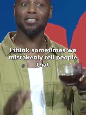 A man with dark skin is centered in front of a camera, dressed in a casual attire, holding a glass with a dark liquid. Overlay text appears above him. The background has some red and blue accents.