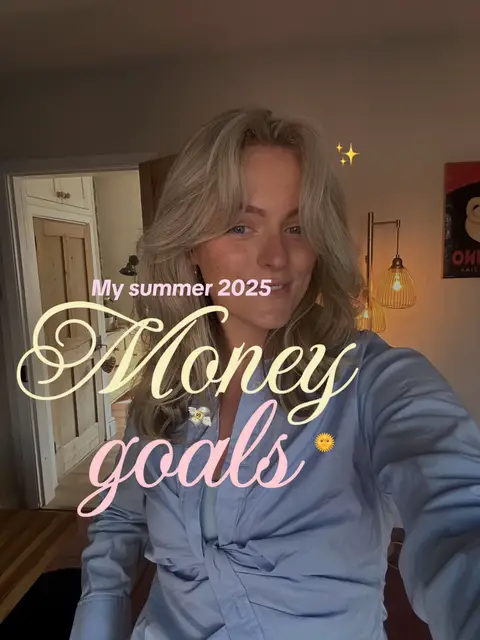 A selfie-style shot featuring a woman with blonde hair. She is smiling in a soft-lit interior space. Overlaid text includes "My summer 2025" in a stylized script and the words "Money goals" in a pink font with a stylized sun emoji. The composition is warm and inviting, with subtle lighting and a focus on the woman's face and the playful text elements.