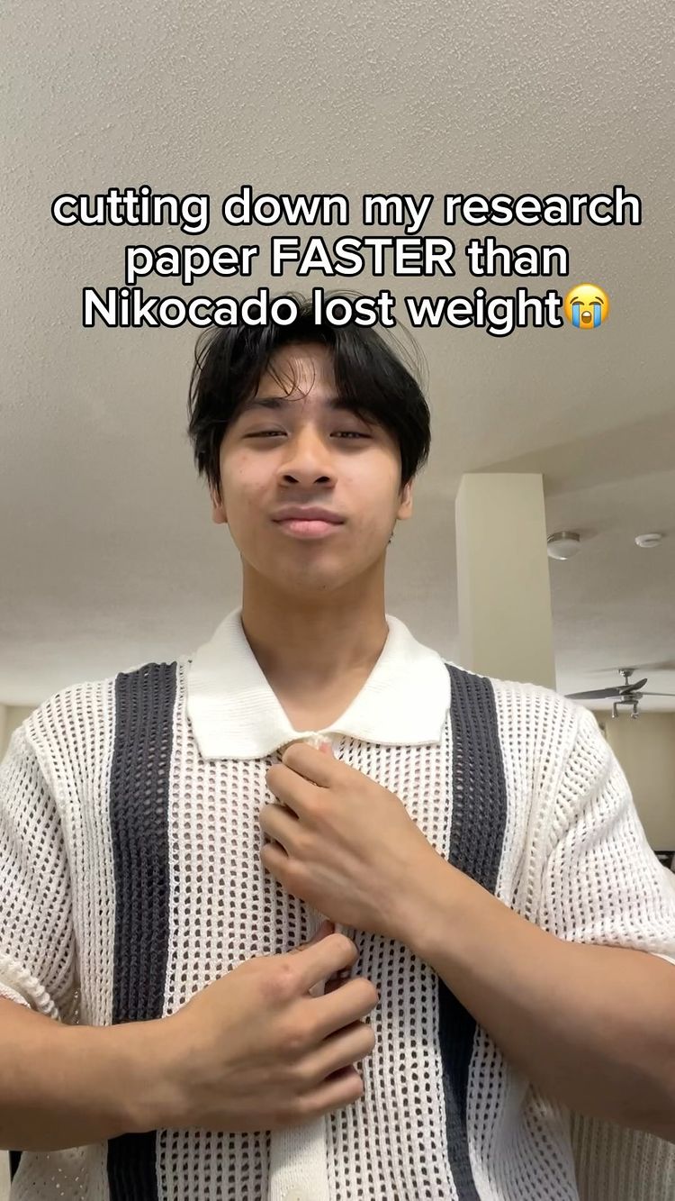 A young man in a white and dark grey patterned sweater is the central figure against a light-colored background. The man's hands are positioned near his chest, adjusting his sweater. Above him, text reads 'cutting down my research paper FASTER than Nikocado lost weight'.
