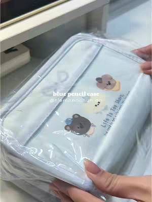 The cover image displays a clear plastic-wrapped pencil case against a background. The pencil case has a light blue color and is decorated with cartoon bear and text graphics. The hand of the person holding the pencil case is visible in the bottom right.