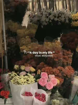 A vibrant photo showcases a profusion of flowers in a flower shop. The composition is filled with a variety of blooms, including roses with deep pink hues, soft yellow chrysanthemums, and white flowers. The flowers are arranged in bouquets and bunches creating a riot of color. Text overlays in the image mention 'a day in my life' and a tiktok username, indicating the video's theme. The overall image is warm and inviting, suggesting a focus on daily life or a shop experience.