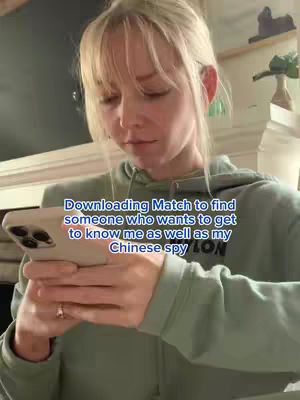 A young woman with blonde hair and bangs is looking down at her phone in this vertical shot. She is wearing a light green hoodie. Text overlay in blue font in the lower center of the frame.