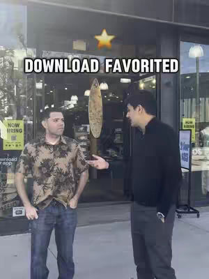 Two men are standing outside a shop with a glass front and multiple signs. One man is wearing a floral shirt and jeans, the other is wearing a black shirt and grey pants. A star icon is placed above the overlaid text, that reads 'DOWNLOAD FAVORITED'.