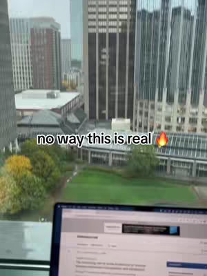 A view from a high-rise window overlooking a city. The foreground shows a laptop screen displaying text, with the city skyline visible through the window. The text overlay says no way this is real.
