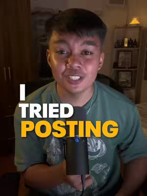 A young man with dark hair and a green shirt is centered in a dimly lit room. A microphone is held in front of his mouth as he looks directly at the camera.  The image has overlayed text in the bottom half that reads 'I TRIED POSTING' in large, bold, white and orange block letters. The background is out of focus suggesting a casual setting.