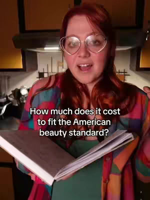 A woman with red hair and heart-shaped glasses is holding an open book. Text overlayed on the image asks "How much does it cost to fit the American beauty standard?" The background is a kitchen setting.