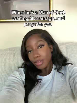 A woman with long black hair and light makeup gazes directly at the camera while sitting on a light-colored couch. Text overlayed over her head reads: When he's a Man of God, waiting till marriage, and prays for you. In the background is a light-colored wall with a painting.
