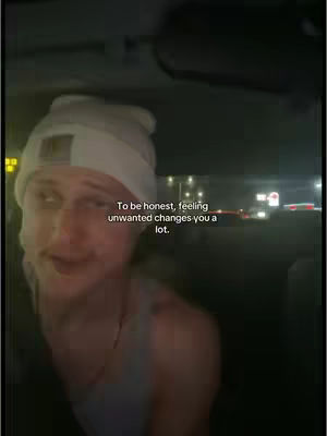 A man with fair skin and light hair is the central focus, with the interior of a car in the background. The man is wearing a white beanie and a gray undershirt. Text overlay is visible on the image.