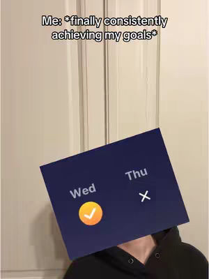 A person with a black hoodie covers their face with a phone screen displaying a calendar. The screen has the word "Wed" with a checkmark and "Thu" with an "X." The background appears to be a light-colored door with vertical paneling.