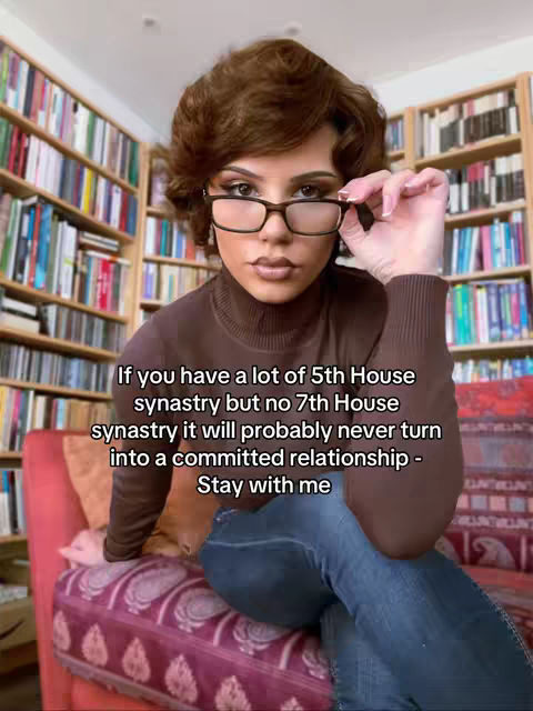 A woman with short, styled brown hair and glasses is seated on a patterned red chair in front of a bookshelf. She is holding her glasses with a slight smile. Text overlays the image providing astrological insights.