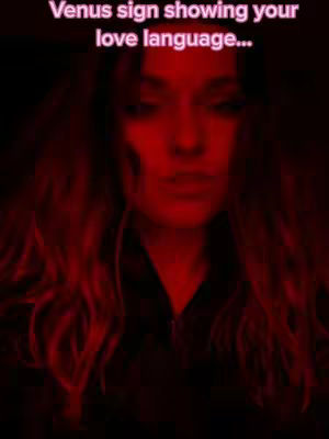 A close-up shot of a person's face, bathed in red light. The person has long, wavy hair that frames their face. The text 'Venus sign showing your love language...' is displayed above the person's head in a light pink color. The overall composition is dark and creates a mysterious atmosphere.