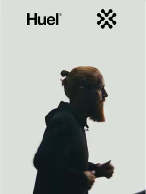 The cover image features a man in profile, viewed from the side. He has a top knot hairstyle and a thick, reddish-brown beard. He is wearing a black hoodie. The background appears to be a plain, light gray color. The Huel product logo is in the top left corner, of the image.