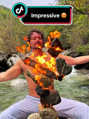 A man sits in a river with stacked stones on fire in front of him and a hook overlay on top.