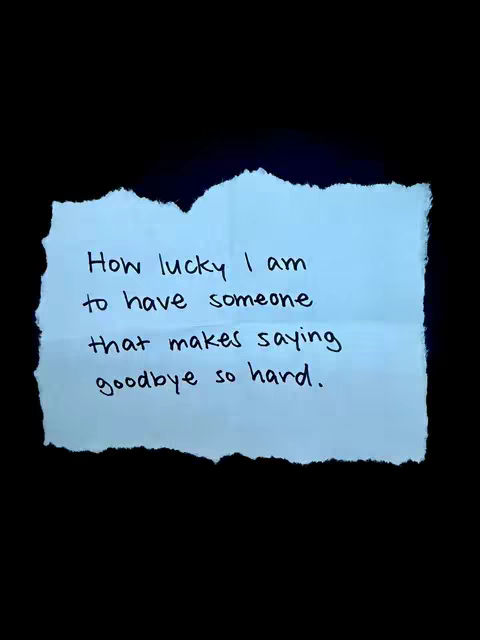 A close-up shot on a black background featuring a torn light blue paper with handwritten text. The paper has rough, irregular edges, suggesting it has been ripped from a larger sheet. The text is in black ink and reads: 'How lucky I am to have someone that makes saying goodbye so hard.' The composition is simple, with the stark contrast between the light blue paper and the black background drawing attention to the message.