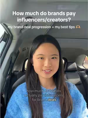 A young woman with long dark hair smiles directly at the camera while sitting in the driver's seat of a car. Text overlay appears on top with question about brands pay influencers/creators with a short description of the content. The car's interior surrounds the woman, visible out of focus