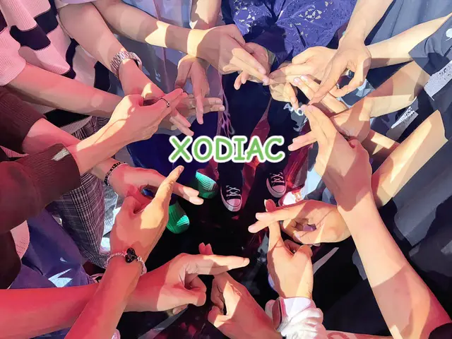 The image shows a group of hands forming a circle, with each hand making a different hand gesture. In the center, the word "XODIAC" is written in a green and white font.