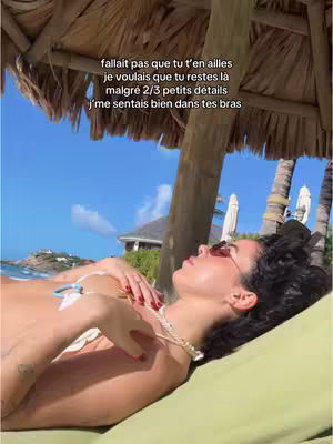A woman lies on a lounge chair, under a sun umbrella, bathed in sunlight. The composition is relaxed and summery, with a focus on the woman.