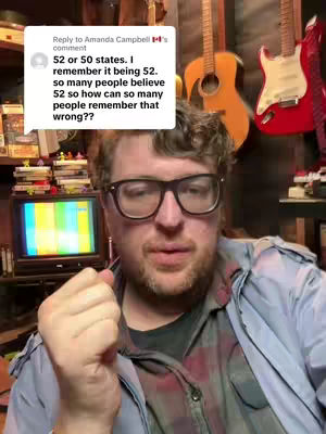 A man with glasses is centered in the frame, holding a pen. A bubble from a comment is situated above his head to the left. The background features guitars and a small television. The man is looking toward the viewer.