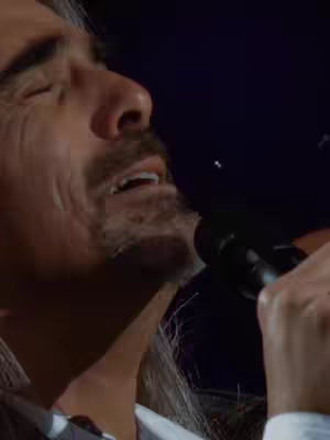 A close up shot of a man singing into a microphone. The person's eyes are closed, and he appears to be deep in song or emotion. The background is dark, which emphasizes the person in the shot.